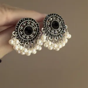 Primer plano de pendientes vintage con circonita negra y detalle de borlas perlas