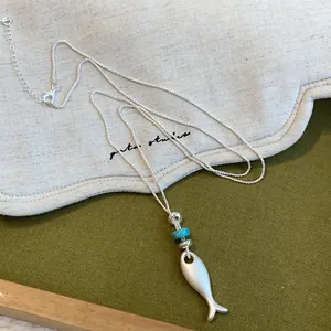 Gros plan détaillé d'un collier pendentif poisson en argent mat avec petite perle bleue décorée