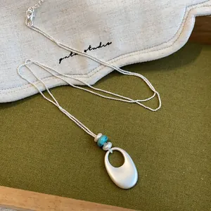 Vue détaillée du collier pendentif ovale en argent mat avec un accent de perle turquoise