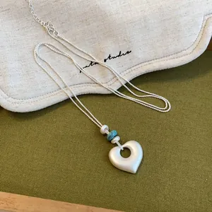 Détail d'un collier pendentif cœur en argent mat avec perles turquoise sur tissu