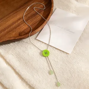 Gedetailleerde close-up van de groene knoop en kwastjes aan de zilveren Y-vormige ketting