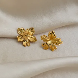 Primer plano de pendientes con forma de flor dorada sobre tela de seda beige