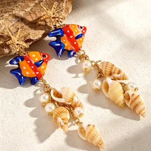 Gros plan de boucles d'oreilles poisson tropical avec glands en coquillage et perles.