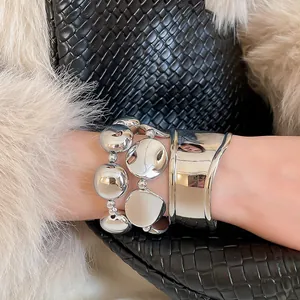 Dettaglio di polsino in metallo irregolare argento e bracciali stratificati