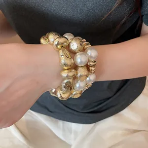 Primo piano di un set di braccialetti a strati con perle bianche e perline d'oro testurizzate