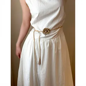Detailed view of bohemian brown braided belt with floral charm and tassels on white dress.