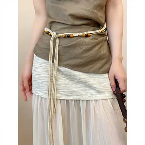 Close-up detail of a Bohemian woven waist belt with natural wooden beads on a model.