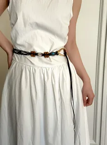 Detail view of a bohemian waist chain belt with wood beads and a shell on a white dress