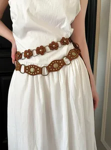 Detail view of two bohemian brown flower and studded waist belts styled on a white dress.