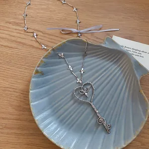 Primer plano de un colgante de llave de corazón con perlas sobre un plato con forma de concha