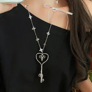 Vista detallada de un collar de perlas con llave de corazón plateado en camisa negra