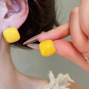 Close-up detail of yellow square sugar bean stud earrings with a glossy enamel finish