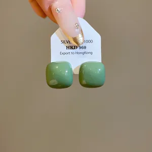 Close-up of glossy green square stud earrings on white display card