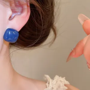 Macro view of a minimalist glossy blue square enamel sugar bean stud earring on ear