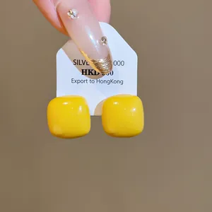 Detail shot of vibrant yellow cube stud earrings with a glossy enamel finish