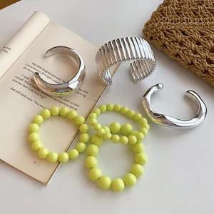 Collection of chunky silver bangles and yellow beaded bracelets displayed on an open book