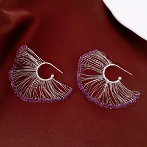 Detalle de pendientes hechos a mano en forma de abanico con cuentas moradas y hilo de plata