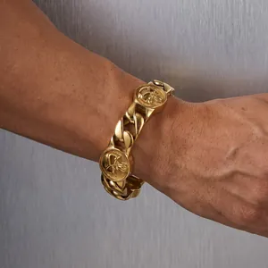 Primo piano di un bracciale a catena cubana dorata da 22mm con teschi in rilievo al polso.