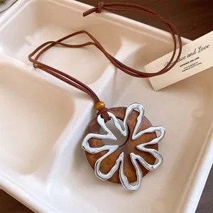 Detalle de collar circular de madera con colgante de flor metálica plateada y cordón.