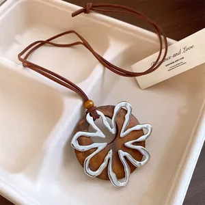 Primer plano de un colgante circular de madera con flor de metal plateado en un cordón.