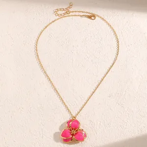Detalle de un collar vintage con colgante de flor de esmalte rosa y cadena dorada