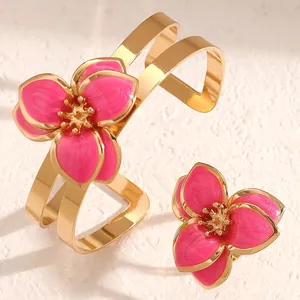 Vista detallada de conjunto de brazalete y anillo dorados con flores de esmalte rosa
