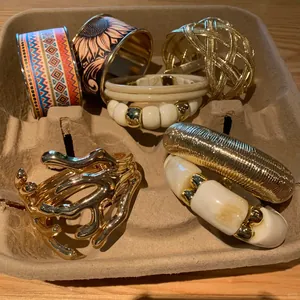 Varietà di braccialetti d'oro bohémien e geometrici presentati in una confezione di carta pesta.