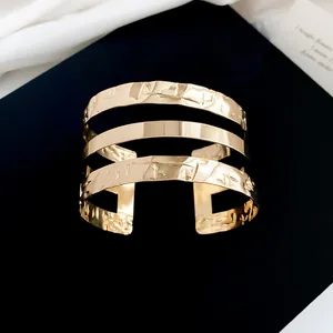 Detailopname van een brede gouden manchetarmband met een unieke gehamerde textuur.