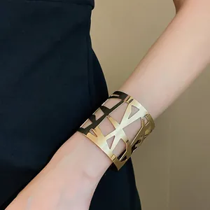 Detailweergave van een brede gouden manchetarmband met geometrisch opengewerkt design op arm