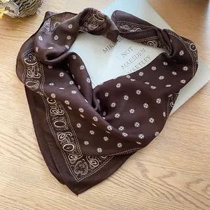 Détail du motif paisley marron sur un foulard en soie rétro posé sur un livre.