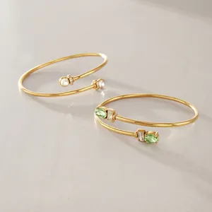 Nahaufnahme von goldenen Edelstahlarmreifen mit grünen und klaren Zirkonia-Edelsteinen.