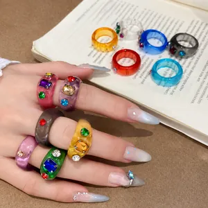 Hand met levendige veelkleurige harsringen met ingebedde edelstenen boven een boek