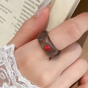 Detailopname van een doorschijnende grijze harsring met een rode strassteen op een vinger.