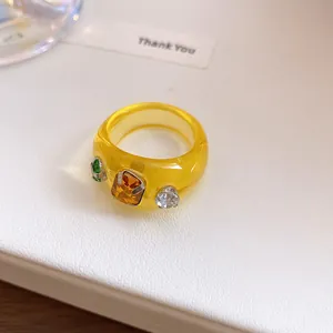 Detailopname van een modieuze gele doorschijnende harsring met kleurrijke strassteentjes.