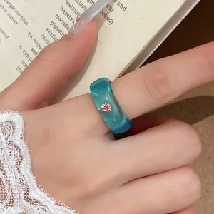 Close-up van een trendy blauwgroene harsring met roze strass-steen aan een vinger