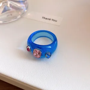 Close-up van een levendige blauwe harsring met drie kleurrijke ingelegde strassteentjes.