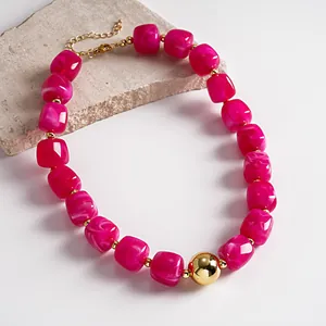 Detailed view of pink marbled acrylic beads and polished gold sphere on a statement necklace