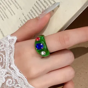 Gedetailleerd overzicht van een groene harsring met gekleurde strass-steentjes op hand.