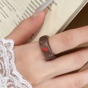 Detailopname van een donkergrijze harsring met een rode strassteen op de vinger.