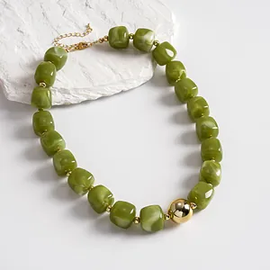 Close-up of olive green marbled acrylic beads and gold sphere on a retro geometric necklace.