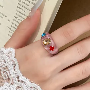 Close-up van een stijlvolle roze harsring met kleurrijke strass-steentjes aan de hand van model.