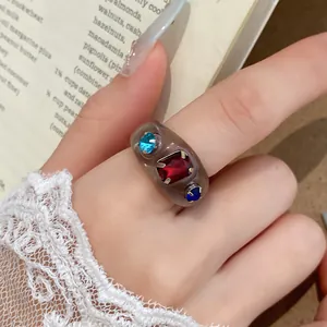 Detailweergave van een grijze harsring met rode en blauwe strassteentjes om vinger.