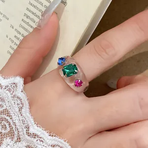 Detailopname van transparante harsring met blauwe, groene en roze steentjes op hand