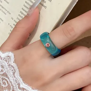 Close-up van een blauwe harsring met een fonkelende roze strass-steen in detail.