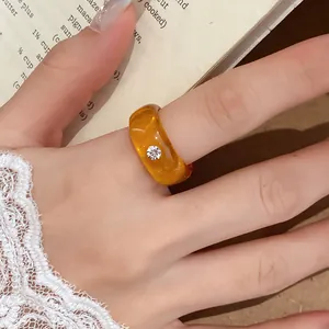 Detail van een amberkleurige harsring met een ingelegde strassteen op een vinger