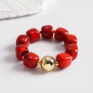 Macro view of marbled red acrylic square beads paired with a shiny gold orb on a bracelet.