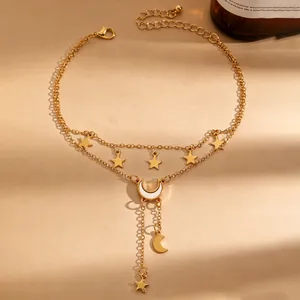 Detail van een goudkleurige gelaagde enkelband met elegante maan- en sterhangers.