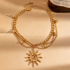 Detailopname van een gelaagde gouden enkelband met een zon hanger en kleine balletjes.