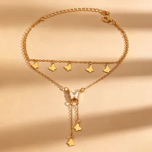 Detail van elegante gelaagde gouden enkelband met witte vlinderhanger en kwastjes