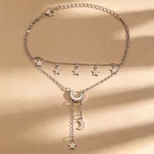 Detailopname van een dubbellaagse zilveren enkelband met fijne maan- en sterhangers.